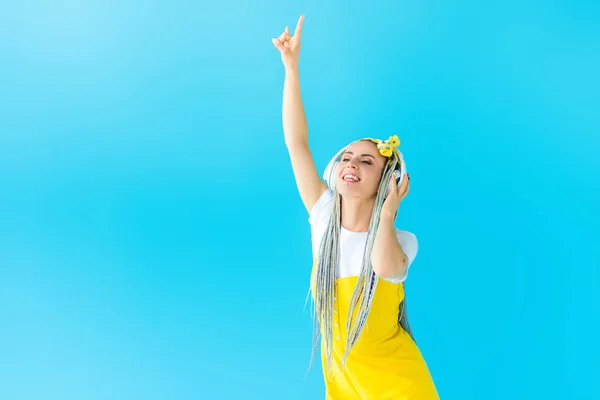 Дівчина з дредлоками в навушниках робить рок знак ізольовано на бірюзовому — стокове фото