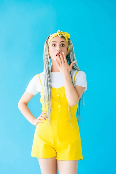 Chica sorprendida con rastas cubriendo la boca aislada en turquesa — Stock Photo