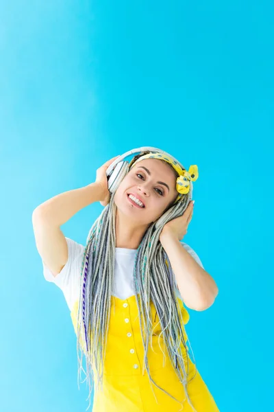 Menina feliz com dreadlocks em fones de ouvido olhando para a câmera em turquesa — Fotografia de Stock