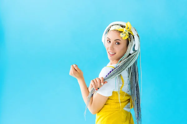 Happy girl with dreadlocks in headphones looking at camera isolated on turquoise — Stock Photo