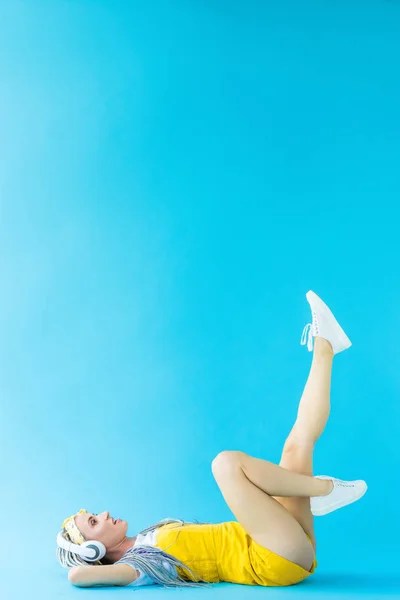 Girl with dreadlocks in headphones lying on turquoise with copy space — Stock Photo