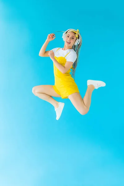 Excited girl with dreadlocks in headphones jumping on turquoise — Stock Photo