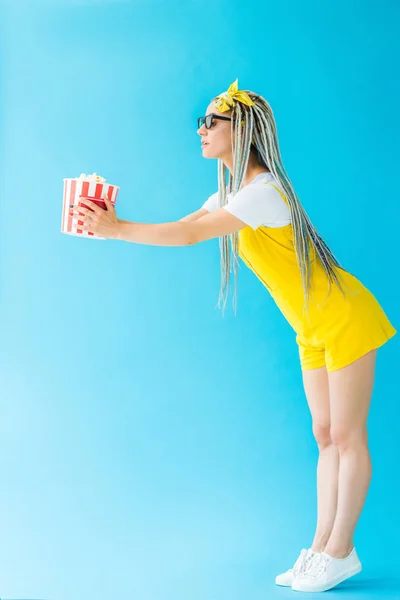 Side view of girl with dreadlocks in 3d glasses holding popcorn on turquoise — Stock Photo