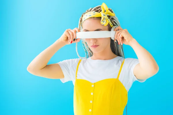 Menina com dreadlocks cobrindo rosto com fones de ouvido isolados em turquesa — Fotografia de Stock