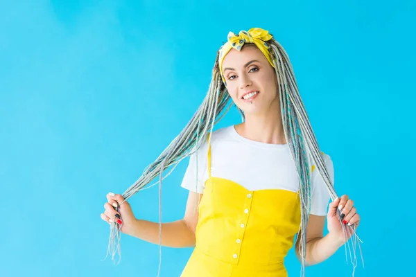 Happy girl with dreadlocks holding hair isolated on turquoise — Stock Photo