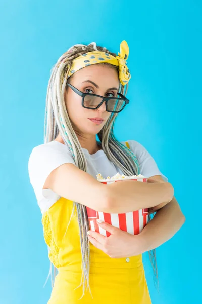 Girl with dreadlocks in 3d glasses holding popcorn isolated on turquoise and looking at camera — Stock Photo