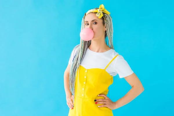 Fille avec dreadlocks et mains sur les hanches soufflant bubblegum isolé sur turquoise — Photo de stock