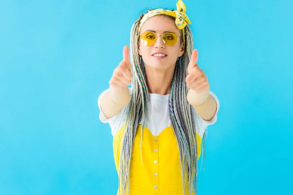 Девушка с дредами в солнцезащитных очках делает большие пальцы вверх изолированы на бирюзовой — стоковое фото