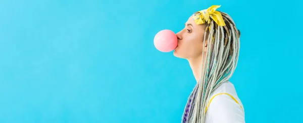 Panoramic shot of girl with dreadlocks blowing bubblegum isolated on turquoise — Stock Photo