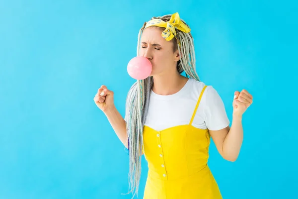 Fille en colère avec dreadlocks et poings serrés soufflant bubblegum isolé sur turquoise — Photo de stock