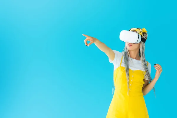 Girl with dreadlocks in virtual reality headset pointing with finger isolated on turquoise — Stock Photo