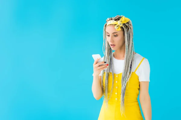 Шокована дівчина з дредлоками за допомогою смартфона ізольована на бірюзовому — стокове фото