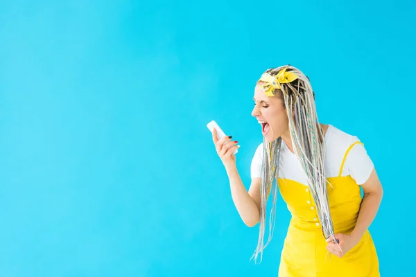Angry girl with dreadlocks yelling at smartphone isolated on turquoise — Stock Photo