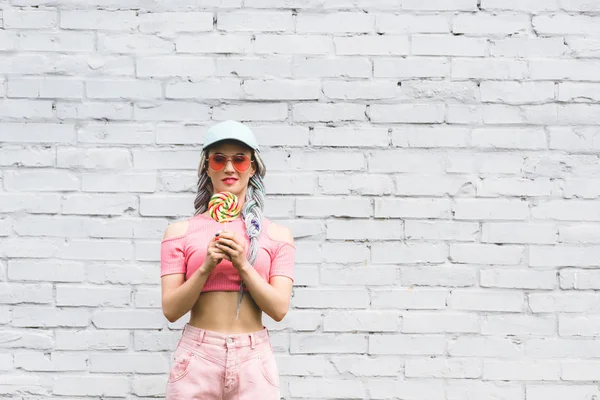 Fille en chapeau et lunettes de soleil tenant sucette près du mur de briques avec espace de copie — Photo de stock