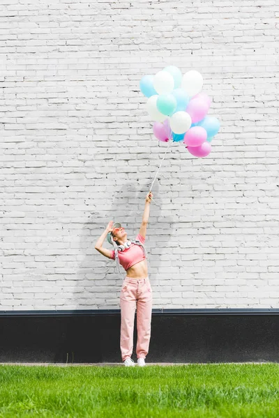 Elegante ragazza in posa con palloncini decorativi vicino muro di mattoni — Foto stock