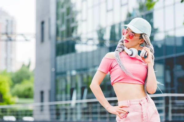 Stylish girl in sunglasses with headphones posing near building with copy space — Stock Photo