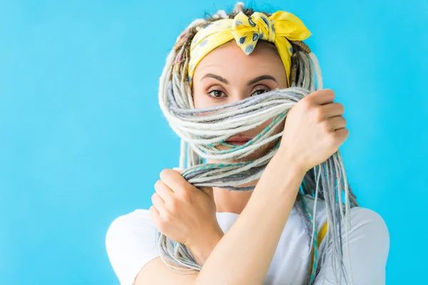 Chica con rastas cubriendo la cara con el pelo y mirando a la cámara aislada en turquesa - foto de stock