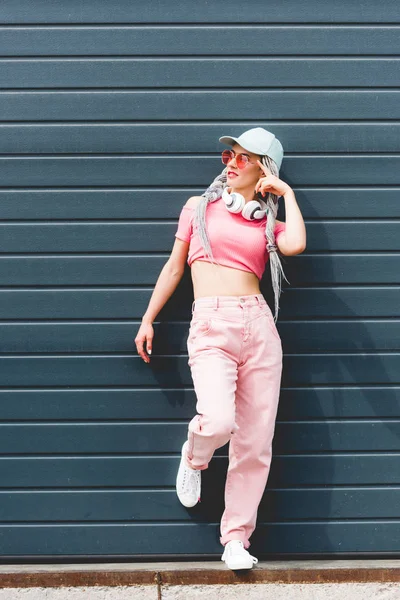 Schöne stylische Mädchen mit Dreadlocks und Kopfhörer posieren in der Nähe der Wand — Stockfoto