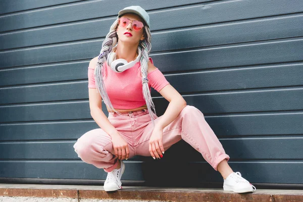 Bela menina elegante com dreadlocks e fones de ouvido posando perto da parede — Fotografia de Stock