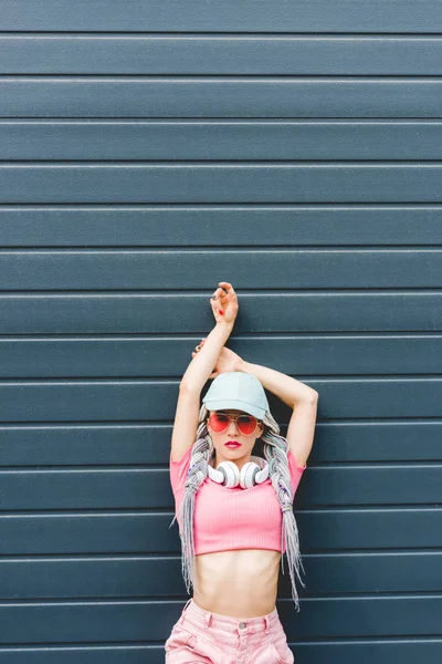 Bela menina da moda com dreadlocks e fones de ouvido posando perto da parede com espaço de cópia — Fotografia de Stock