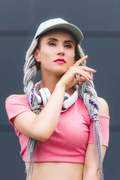 Hermosa chica con estilo con rastas y auriculares mirando hacia otro lado - foto de stock