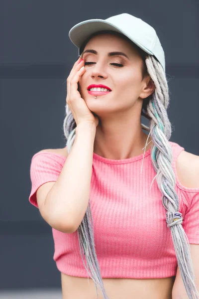 Beautiful stylish smiling girl with dreadlocks in hat touching face — Stock Photo
