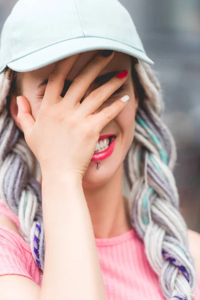 Girl with dreadlocks in hat laughing and covering face — Stock Photo