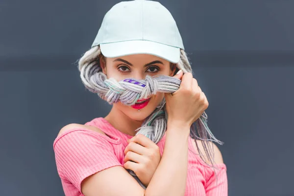 Beautiful stylish girl with dreadlocks in hat covering face with hair — Stock Photo