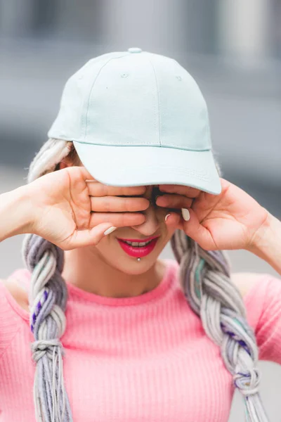 Selektiver Fokus des stilvollen Mädchens mit Dreadlocks im Hut, das die Augen mit den Händen bedeckt — Stockfoto