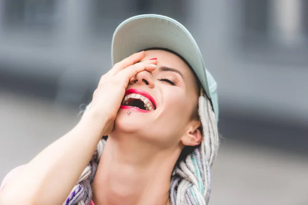 Beautiful girl with dreadlocks in hat laughing and covering face — Stock Photo