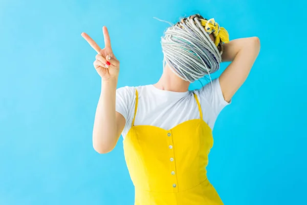 Menina com dreadlocks cobrindo rosto com cabelo e mostrando sinal de paz isolado em turquesa — Fotografia de Stock