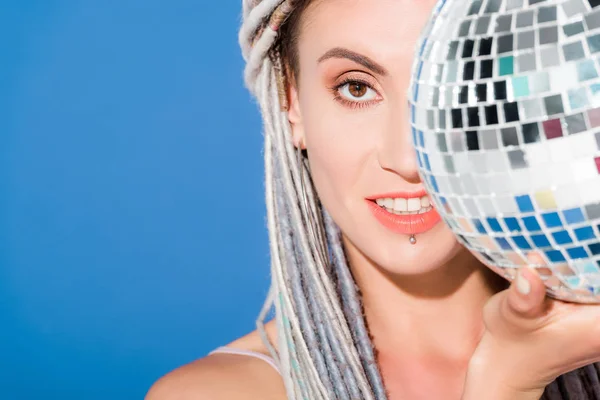 Menina bonita com dreadlocks cobrindo rosto com bola de discoteca isolado em azul — Fotografia de Stock