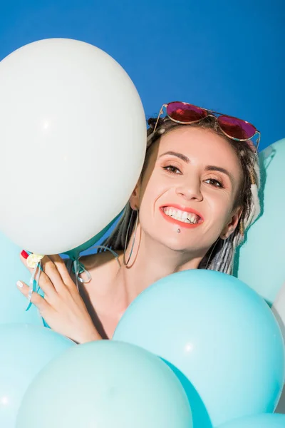 Hermosa chica sonriente posando con globos aislados en azul - foto de stock