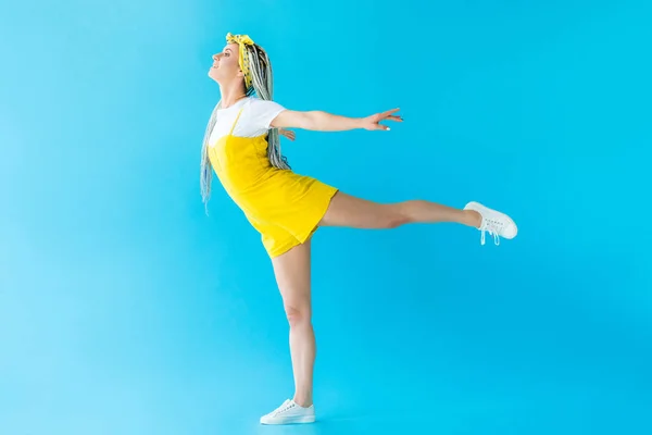 Happy girl with dreadlocks with outstretched hands and leg posing on turquoise — Stock Photo