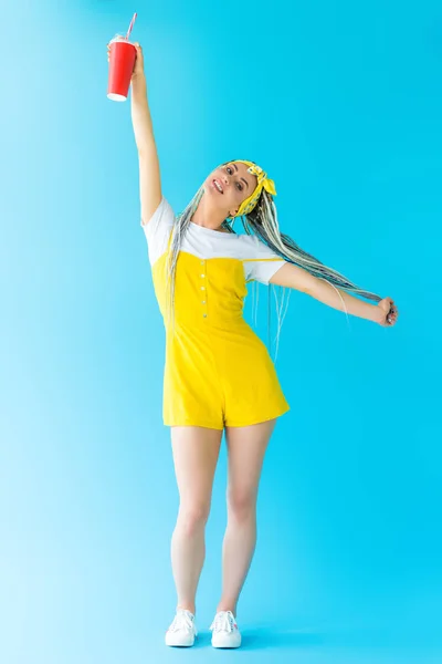 Bela menina feliz com dreadlocks e bebida de refrigerante posando com as mãos estendidas em turquesa — Fotografia de Stock