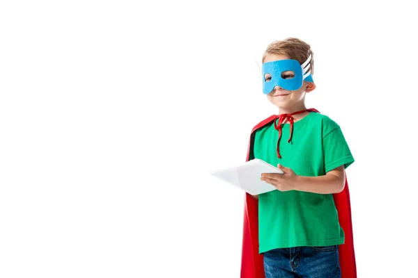 Lächelndes Vorschulkind in Maske und rotem Heldenmantel mit digitalem Tablet auf weißem Hintergrund — Stockfoto