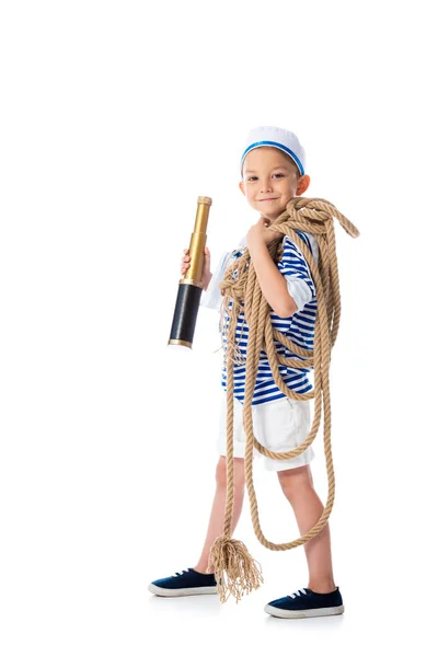 Full length view of smiling preschooler child in sailor costume holding spyglass and rope on white — Stock Photo