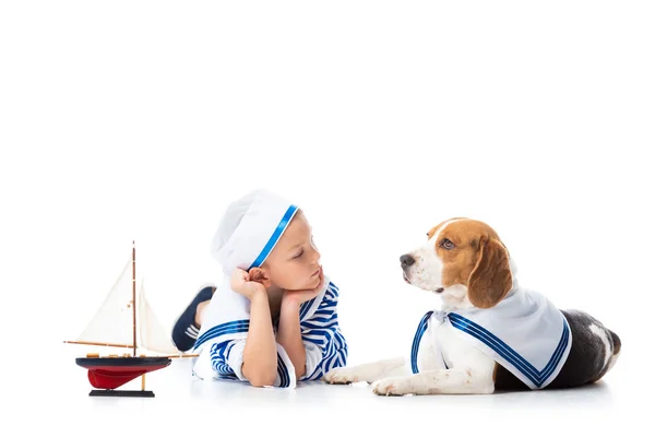 Preschooler child in sailor costume with toy ship and beagle dog on white — Stock Photo