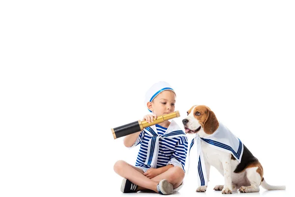 Criança pré-escolar em terno marinheiro segurando spyglass enquanto brincava com cão beagle isolado em branco — Fotografia de Stock