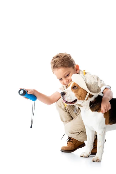 Lächelndes Forscherkind hält Taschenlampe in der Hand und umarmt Beagle-Hund mit Hut auf weißem Grund — Stockfoto