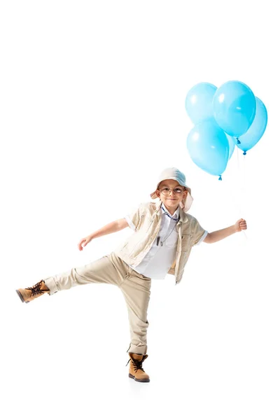 Vista completa del niño explorador en gafas de pie sobre una pierna y sosteniendo globos azules aislados en blanco - foto de stock