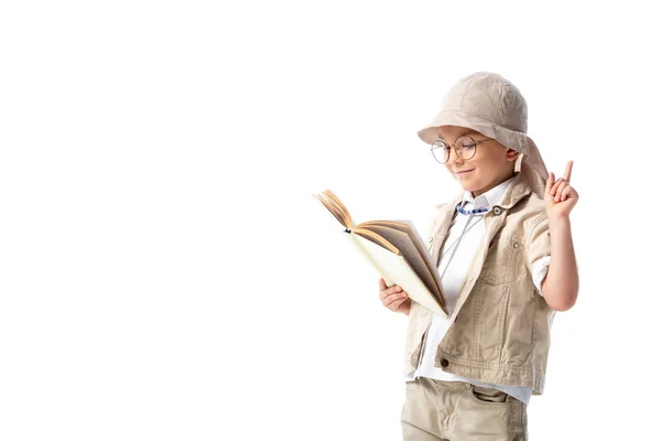 Concentré enfant explorateur souriant dans des lunettes lecture livre et montrant signe d'idée isolé sur blanc — Photo de stock