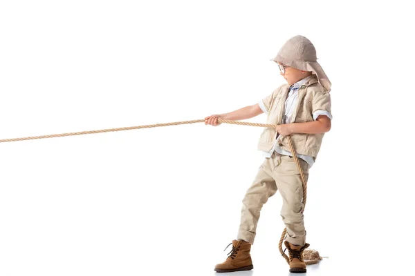 Full length view of focused explorer kid in hat and glasses holding rope on white — Stock Photo