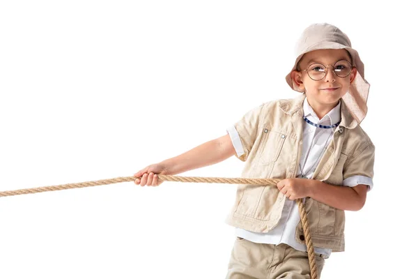 Smiling explorer kid in hat and glasses holding rope and looking at camera isolated on white — Stock Photo