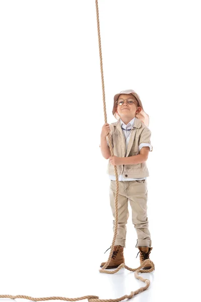 Vista completa de niño explorador sonriente en sombrero y gafas sosteniendo la cuerda en blanco - foto de stock