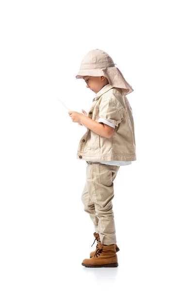 Vista lateral del niño explorador en gafas y sombrero usando tableta digital aislada en blanco - foto de stock