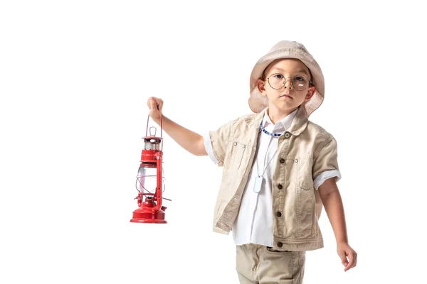 Pensive explorer boy in glasses and hat holding red lantern and looking at camera isolated on white — Stock Photo