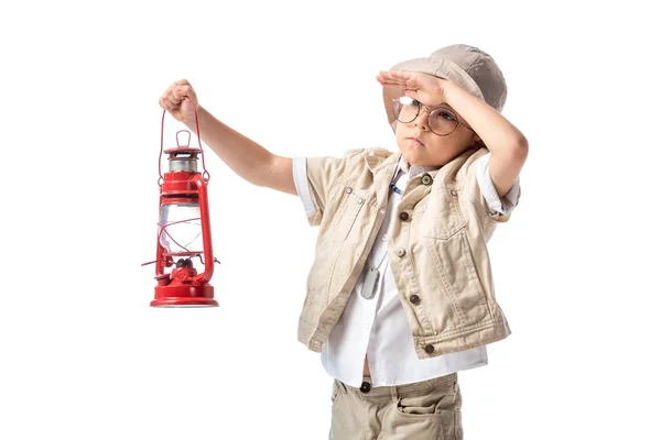 Pensive explorer boy in glasses and hat holding red lantern and looking at distance isolated on white — Stock Photo