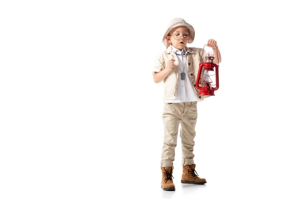 Full length view of explorer boy in glasses and hat holding red lantern on white — Stock Photo