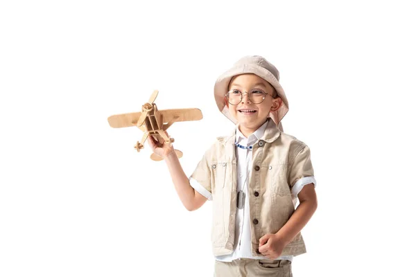 Menino explorador sorridente em óculos e chapéu segurando avião de brinquedo de madeira isolado no branco — Fotografia de Stock